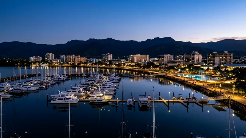 Cairns waterfront skyline at blue hour reflected in still marina water.